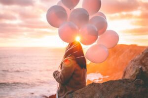 Woman holding balloons watching sunset