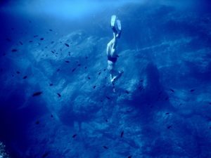 Person free diving down to touch sea bed